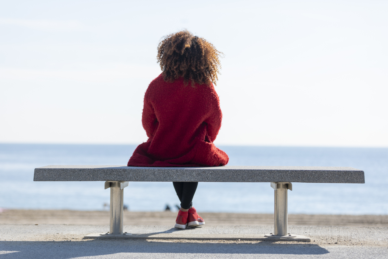 Rear view of a young curly woman wearing red denim jacket sitting on a